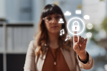 Mulher em um escritório toca um ícone digital de cadeado em uma tela transparente, ilustrando o uso de tecnologia e boas práticas de LGPD e comunicação interna para proteger informações dentro da empresa.